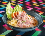 21 Traditional Peruvian cebiche with fish, corn, sweet potato, and red onions in a dark bowl on a colorful table.